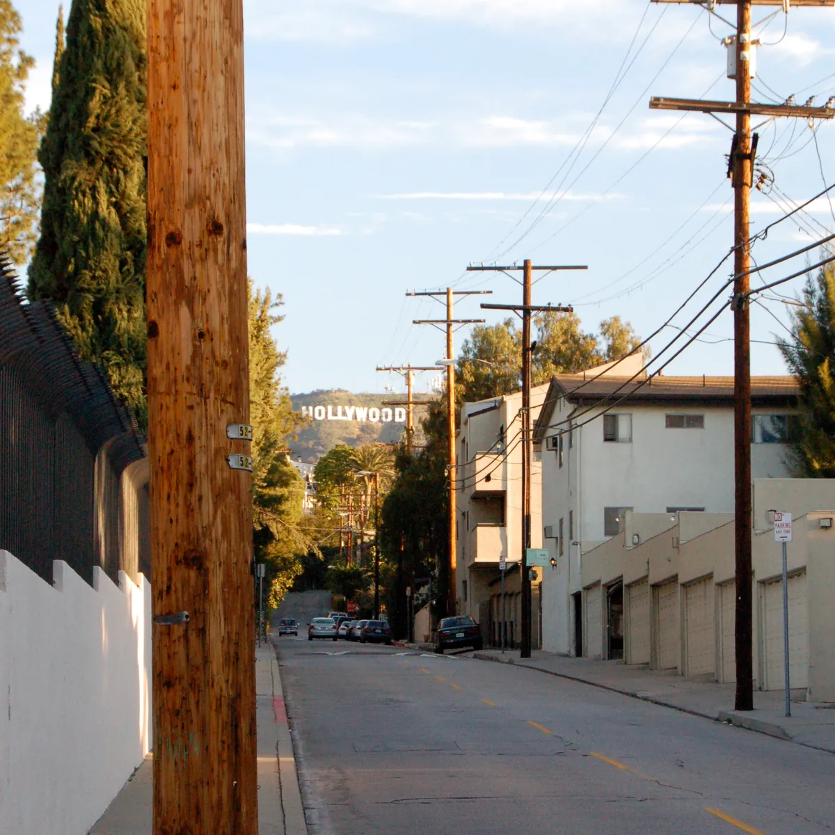 A quiet street with telephone poles leading up to the Hollywood sign.
