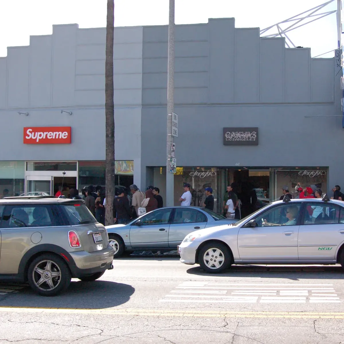The Supreme store front across the street, with the queue and parked cars.