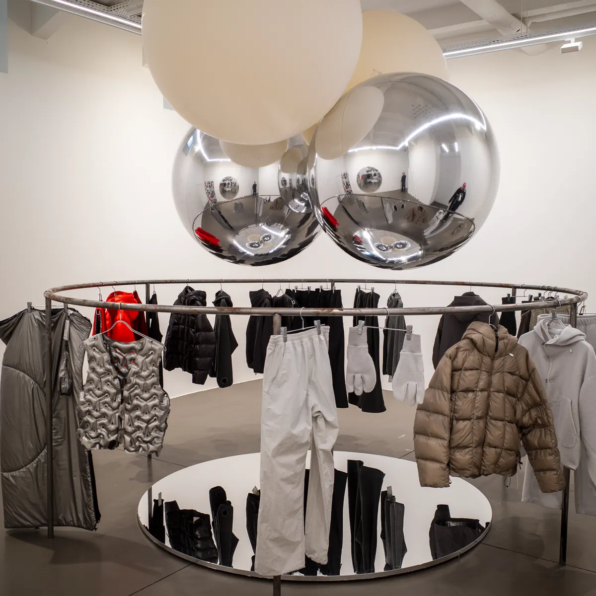 Jackets on a round rail under silver balloons in a white store.