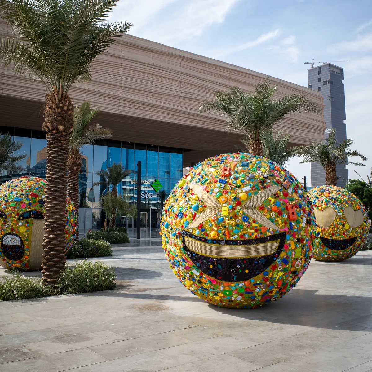 Giant laughing emoji spheres covered in colourful mosaic outside a mall.