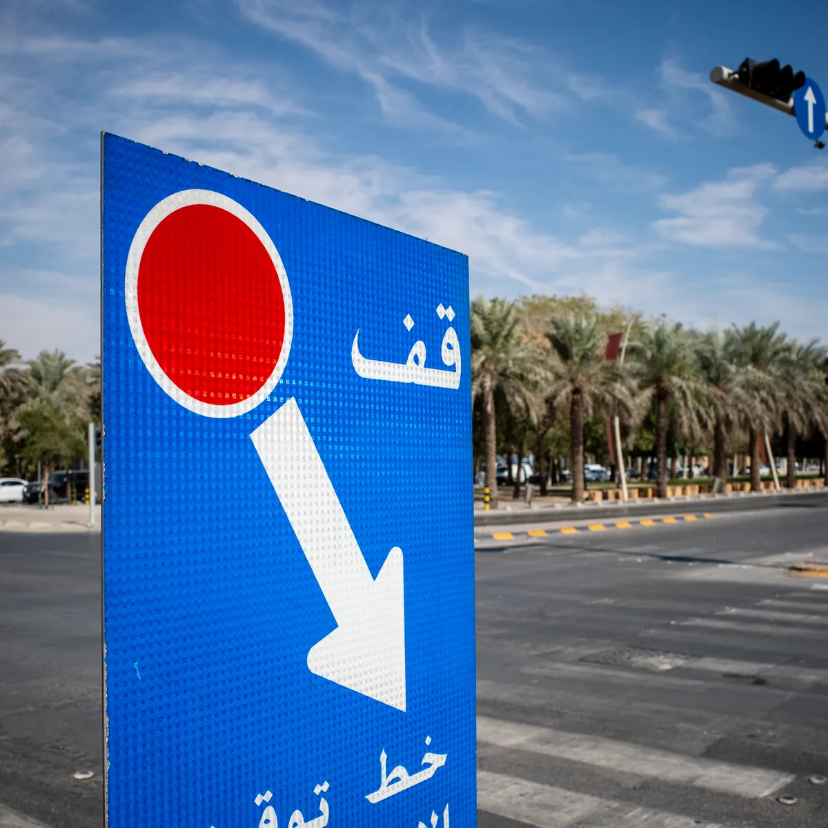 An Arabic stop-line sign by a Riyadh road lined with palms.