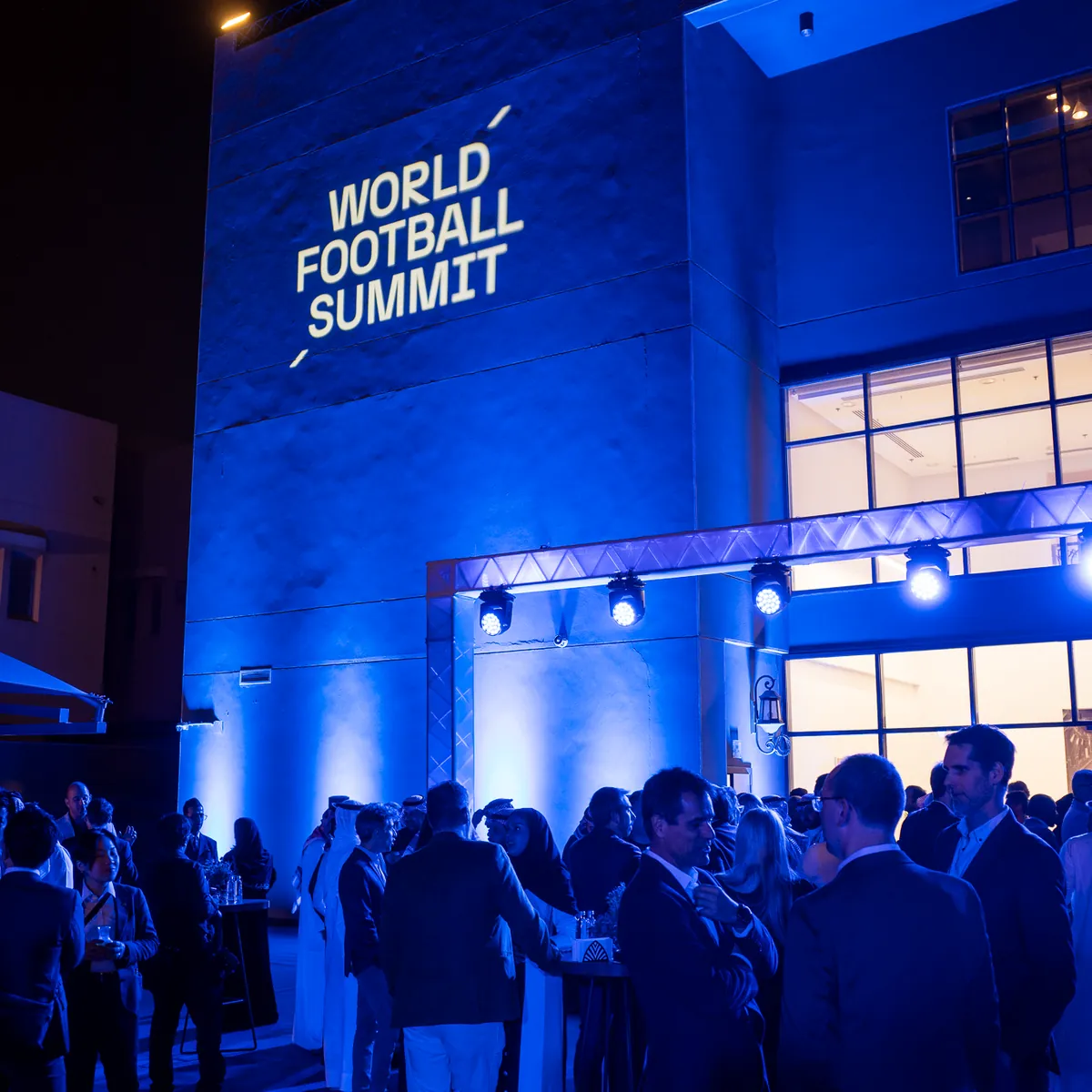Guests outside the World Football Summit, its name lit on a blue wall.