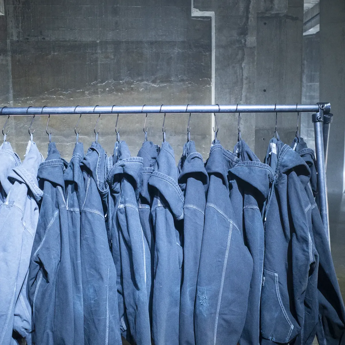 Blue Active Jackets hanging on a rail against a concrete wall.