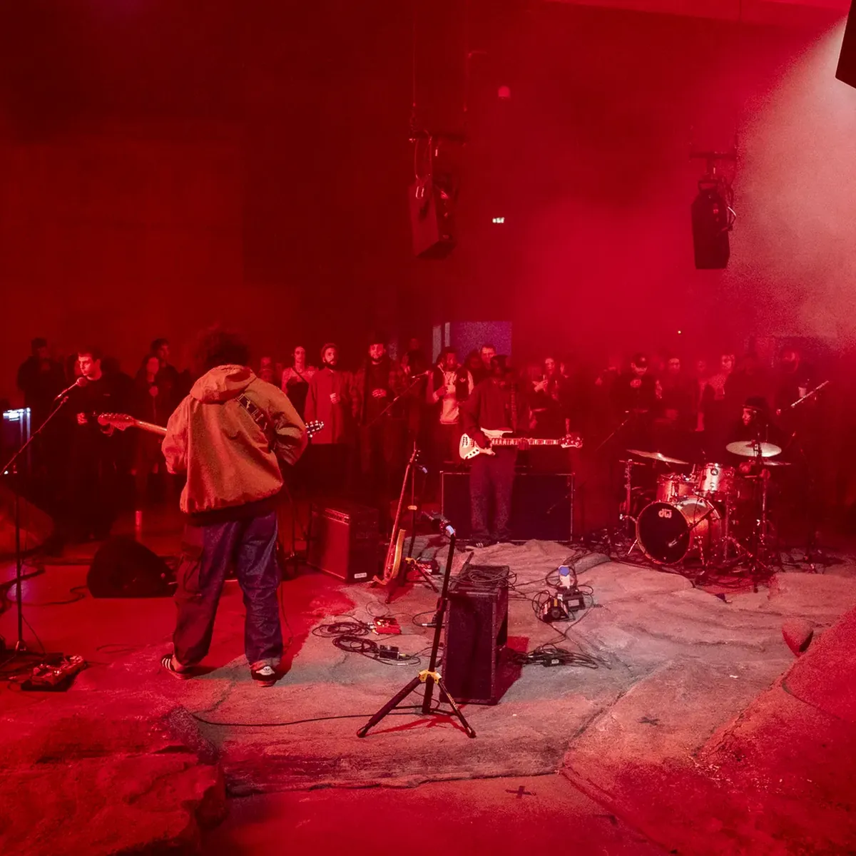 A band playing in red light on the concrete floor.